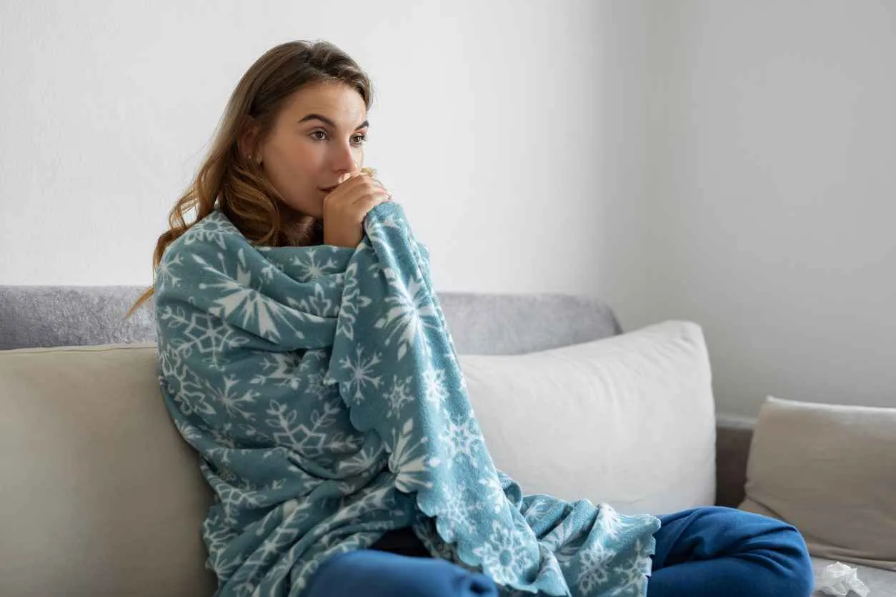 Woman sitting on couch with blanket wrapped around her due to not having any heat at home